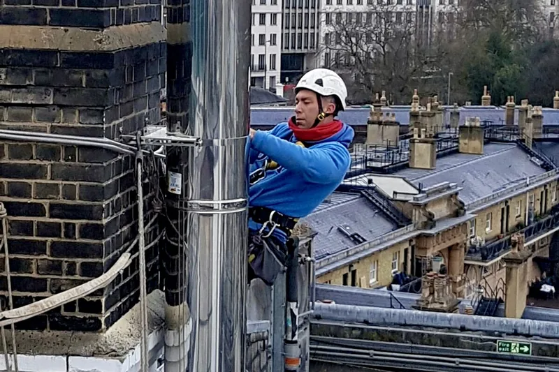 Rope-access engineer fitting insulated twin wall flue system at height